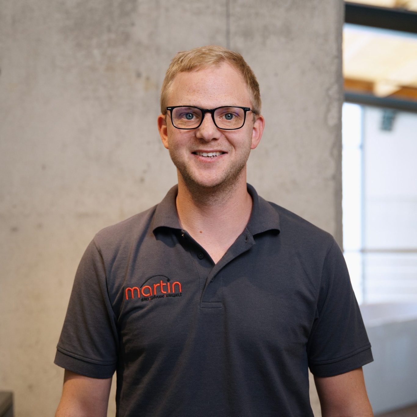 Andreas Lorschiedter Lächelnder Mann mit Brille, trägt ein dunkelgraues Polo-Shirt mit Logo.